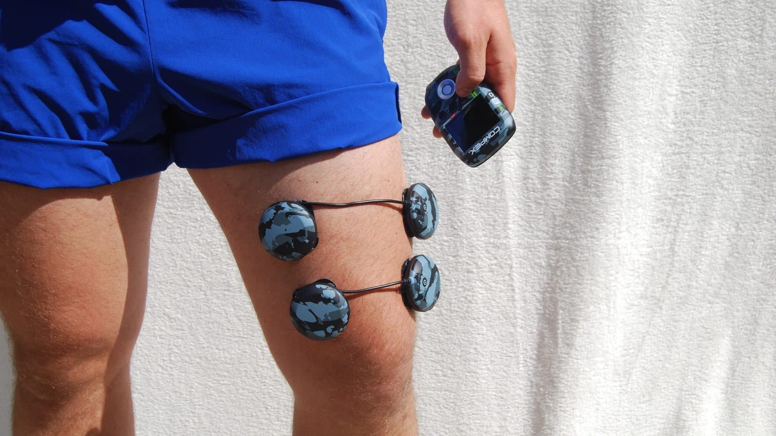 Compex wireless pods on the quadriceps above the knee, with the SP 8.0 control unit in hand
